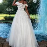 A bride in a long white wedding gown, turned back and striking a pose, standing in front of a small water fountain in an outdoor area surrounded by trees and plants