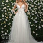 Bride in an ivory white long gown, posing in front of a wall decorated with white flowers and green plants